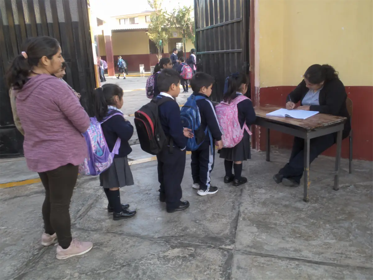 Una auxiliar anota en un cuaderno la hora de entrada de cada alumno, en la puerta de un colegio