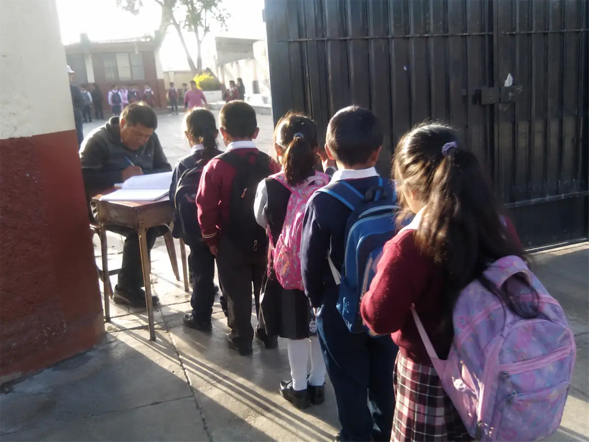 Fila de alumnos esperando mientras el auxiliar anota la entrada en un cuaderno